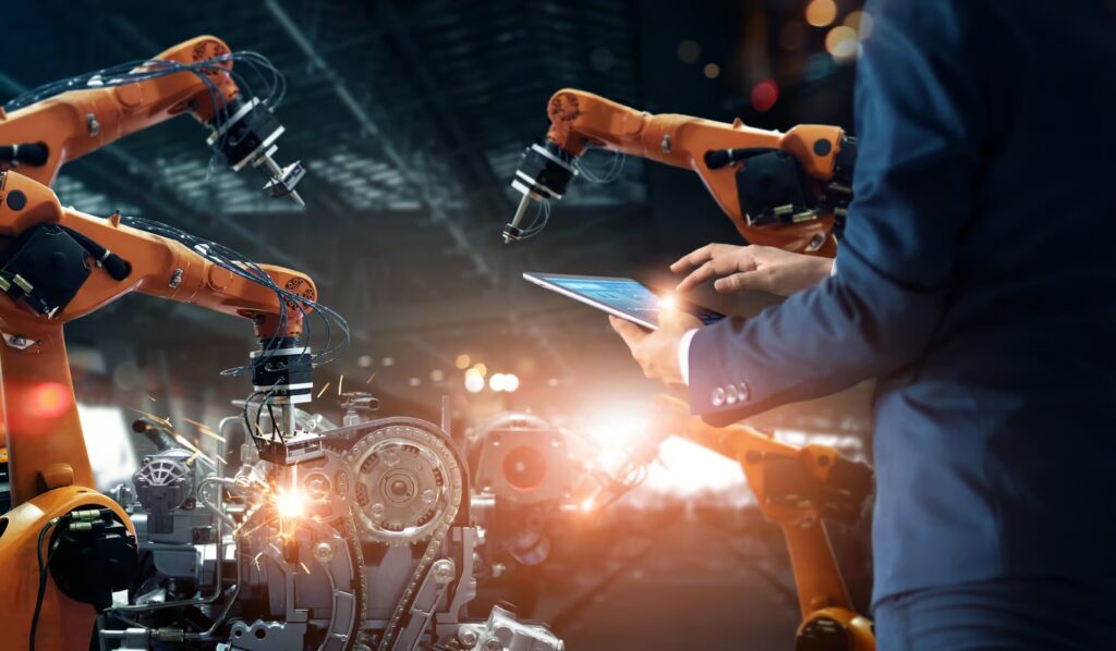 Is Your Testing Stuck in the Past? 5 Signs You Need to Automate 3 A person uses a tablet to monitor and control robotic arms in a high-tech automated manufacturing environment.